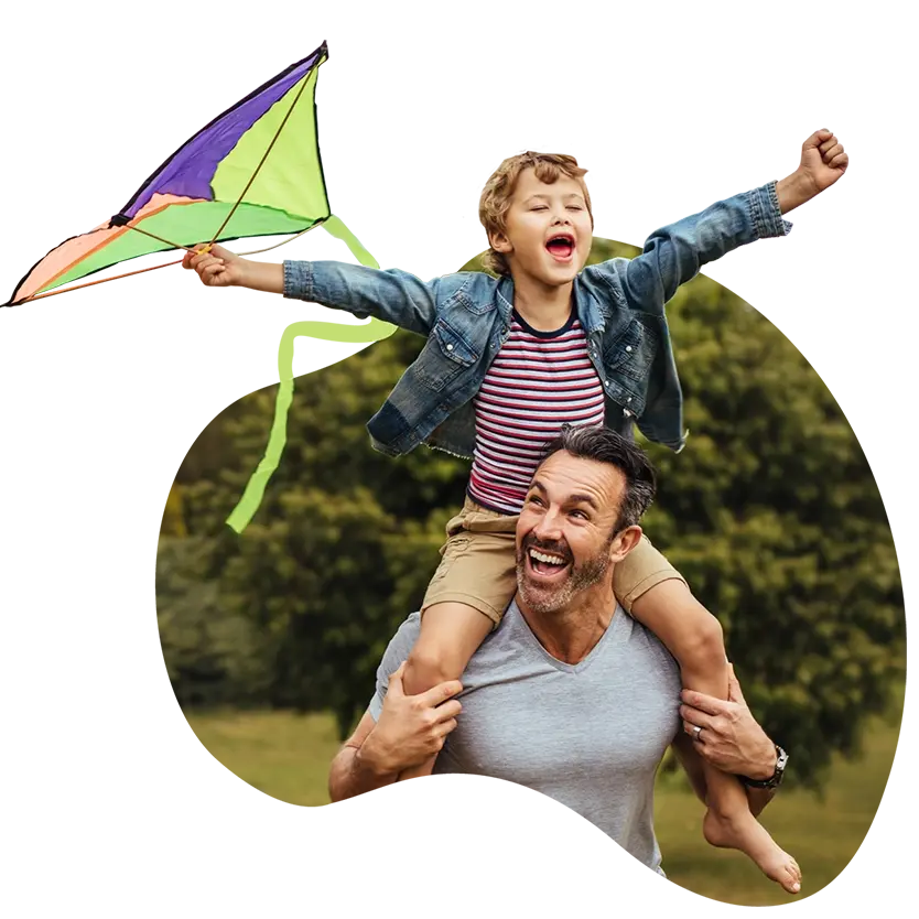 Son riding on his dad's shoulder, flying a kite