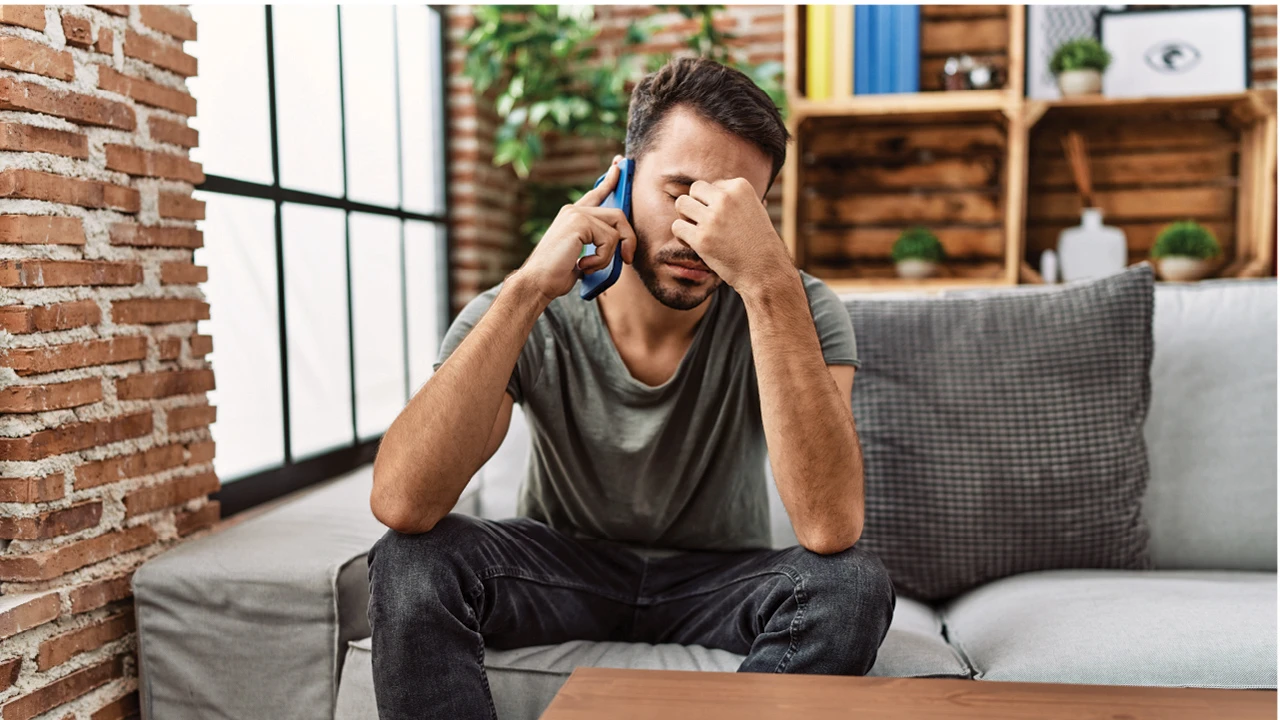 Frustrated man on a phone call holding his head.
