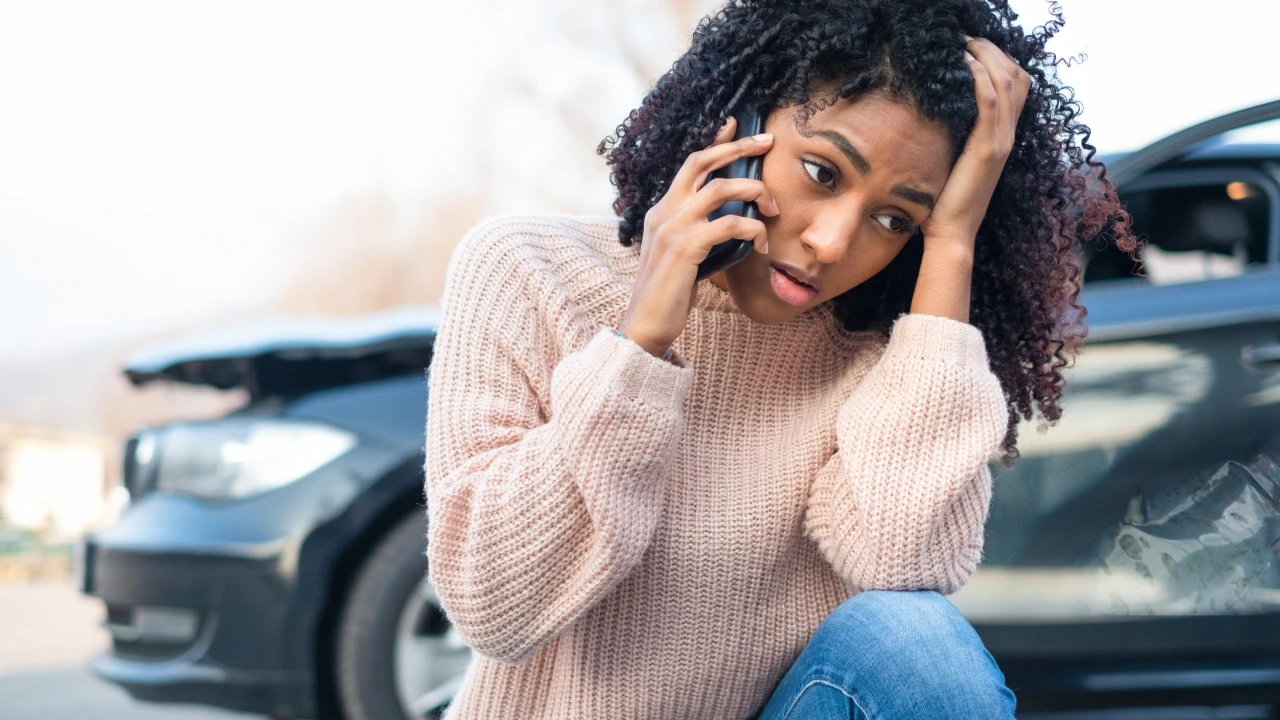 Woman calling for help in front of a damaged car.
