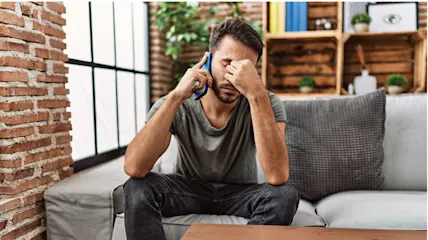 Frustrated man on a phone call holding his head.