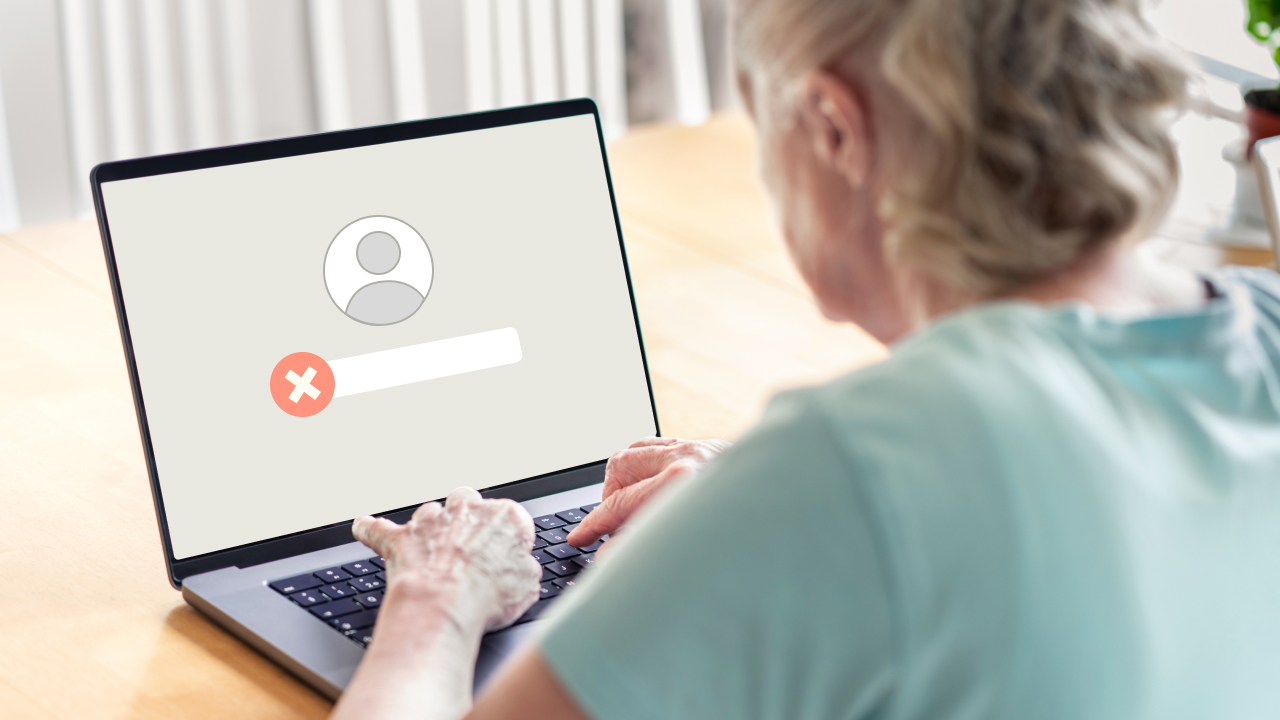 A woman sits at a table and attempts to enter her login to an account that has been taken over by fraudsters. 