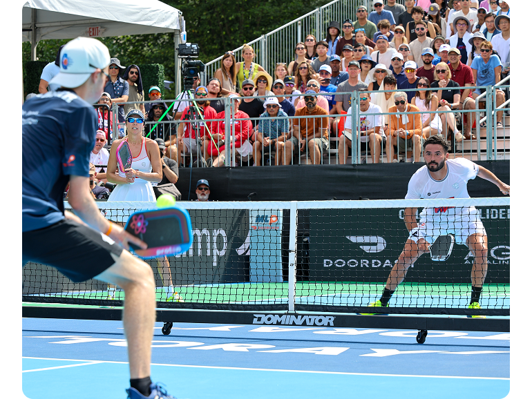 Mixed doubles pickleball player successfully backhands ball to the opposing team. 