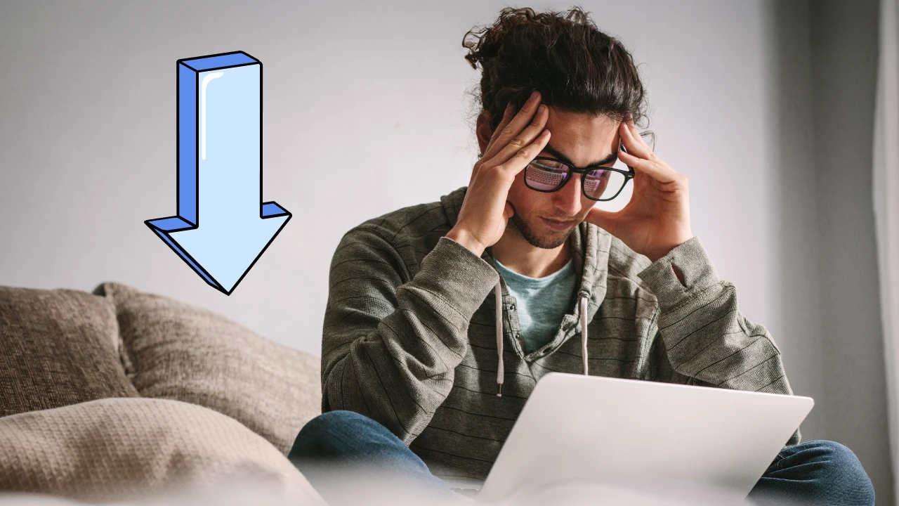 A young person has his head placed worriedly in his hands as he reviews his finances on a laptop. 