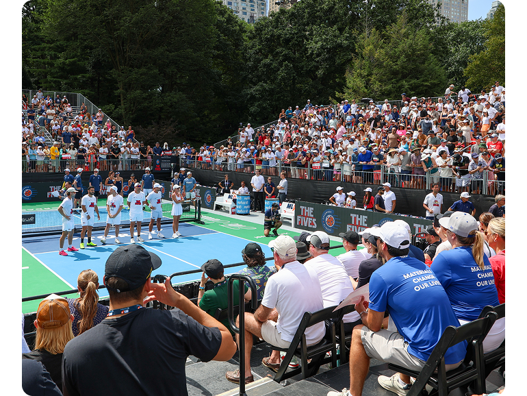 Pickleball players stand on the court surrounded by bleachers filled with spectators. 