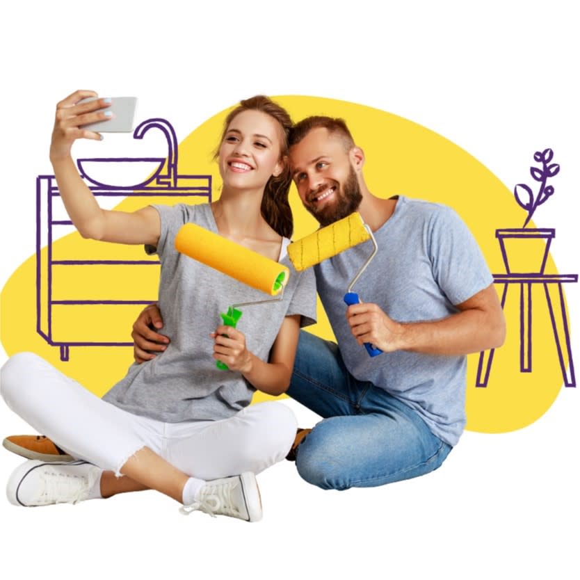 Young couple takes a selfie as they happily hold paint rollers in front of their freshly painted bathroom.
