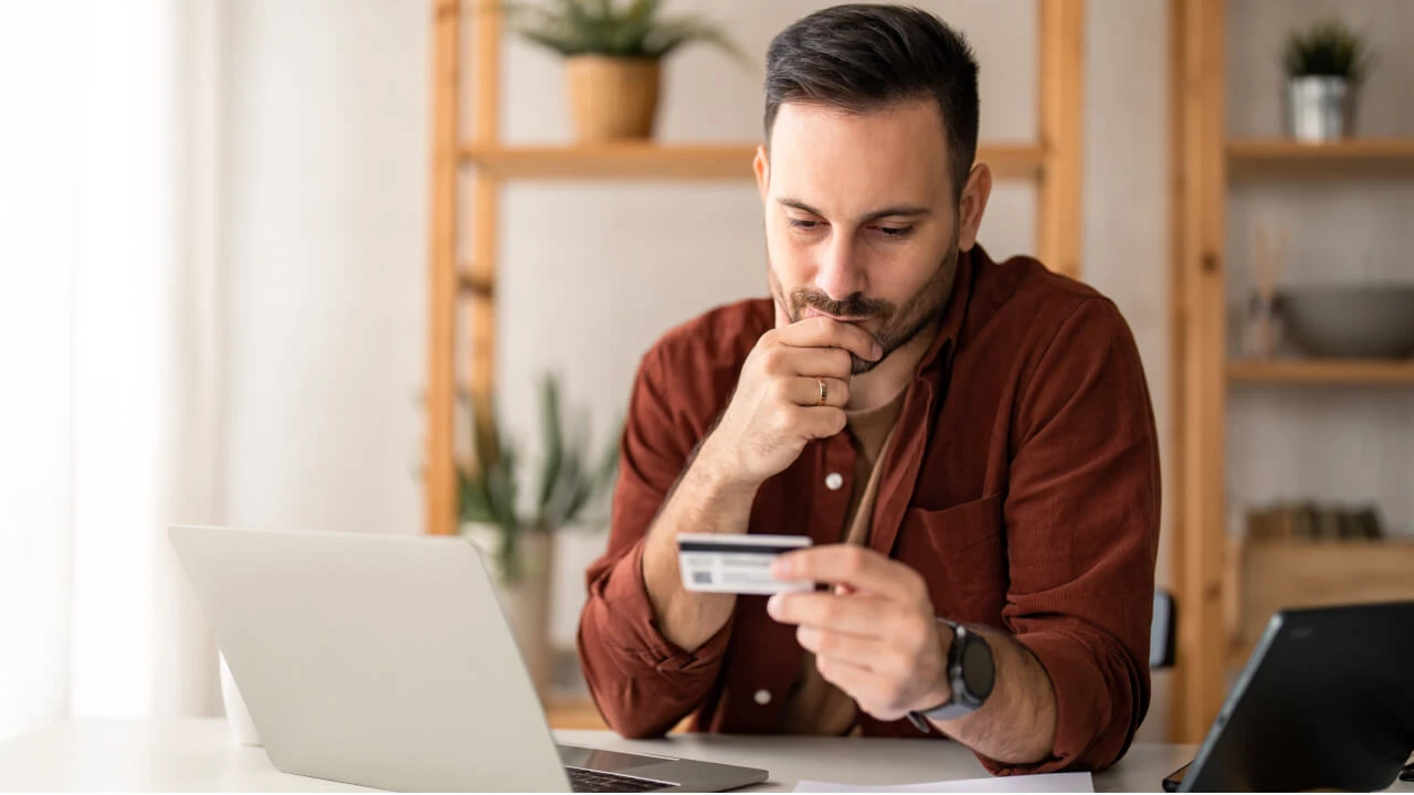 Man sitting at a desk holding a credit card. 