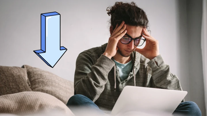 A young person has his head placed worriedly in his hands as he reviews his finances on a laptop. 